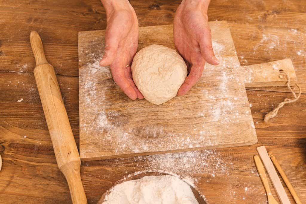 Close-up of hands holding dough on a wooden board with flour.