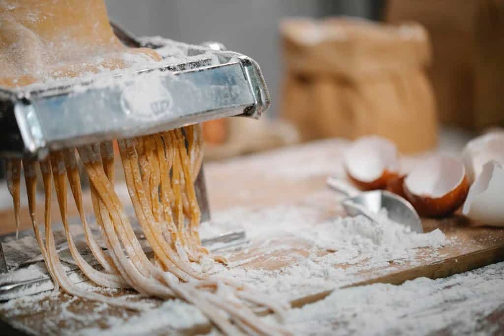 Spaghetti produced from iron pasta cutter on wooden table with eggshell and flour on blurred background