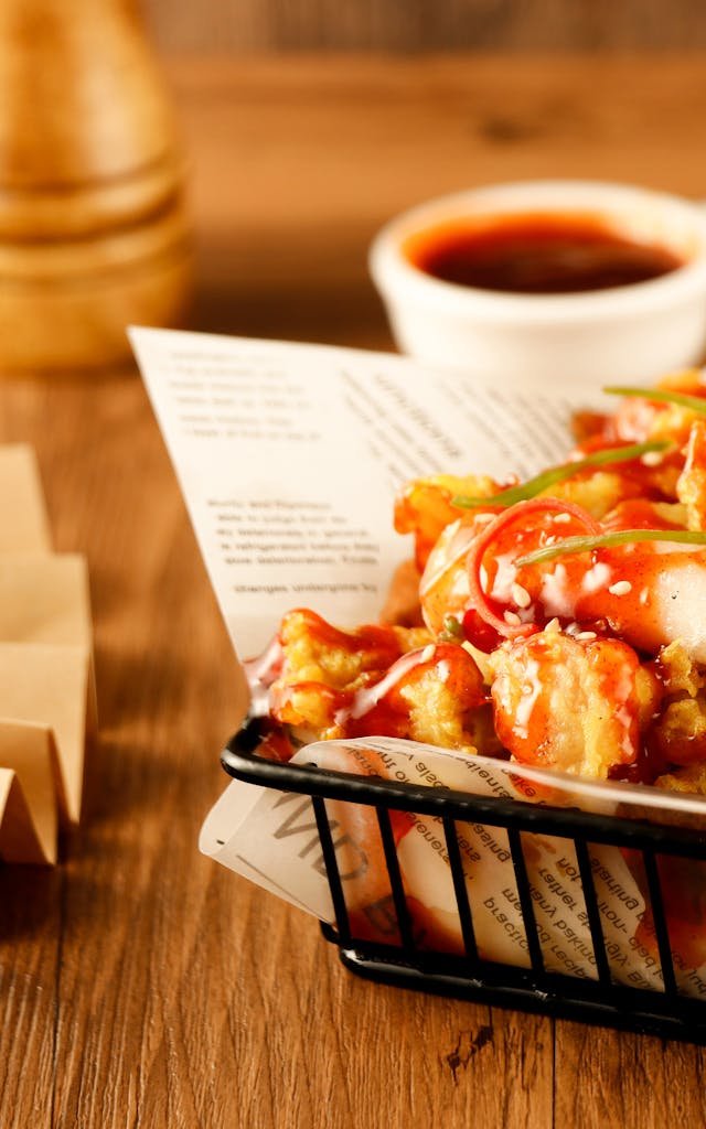 Appetizing crispy chicken served in a basket with a side of swicy glaze recipes dipping sauce.