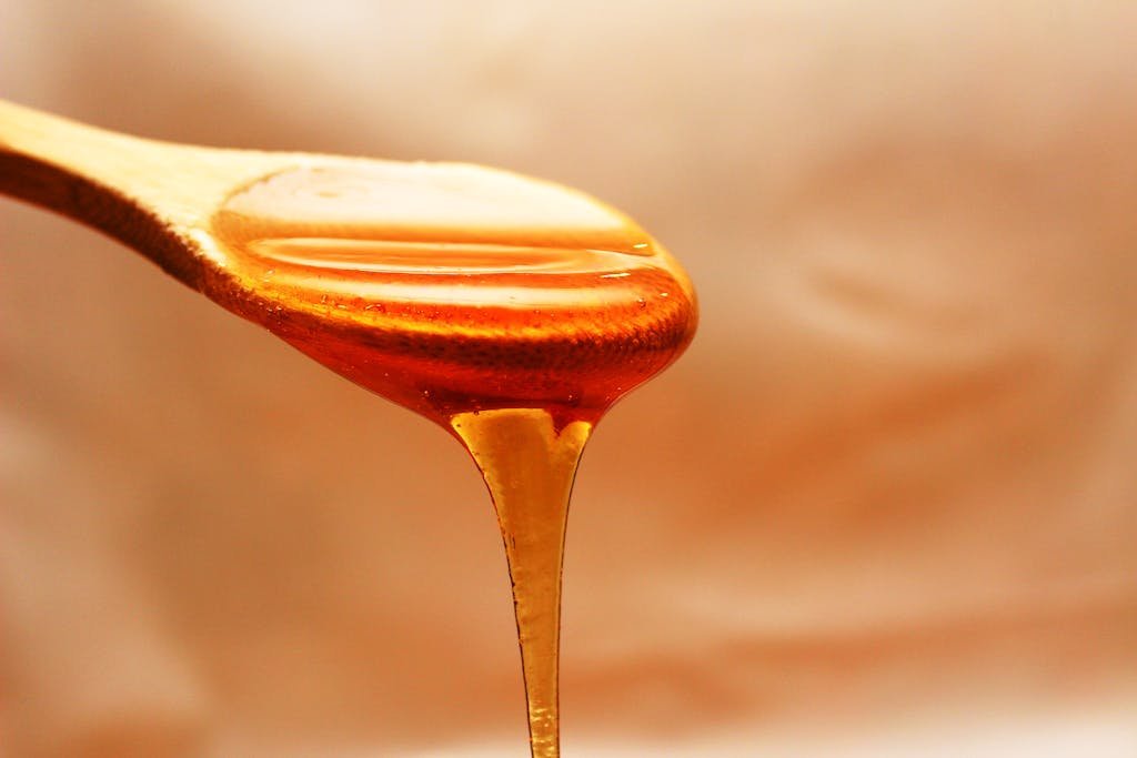 Close-up of honey dripping from a wooden spoon, showcasing its rich texture and color to make a swicy glaze recipe.